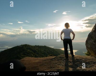 Persone non riconosciute - ragazza in cima montagna guardando paesaggio e diga serbatoio - tramonto retroilluminazione Foto Stock