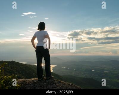 Persone non riconosciute - ragazza in cima montagna guardando paesaggio e diga serbatoio - tramonto retroilluminazione Foto Stock