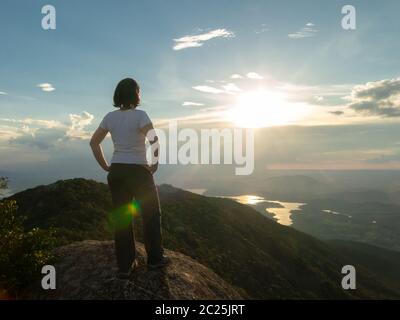 Persone non riconosciute - ragazza in cima montagna guardando paesaggio e diga serbatoio - tramonto retroilluminazione Foto Stock