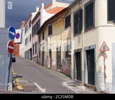 una strada stretta e tranquilla vuota a funchal madeira con vecchie case dipinte su una ripida collina con persiane e cartelli stradali n sole luminoso Foto Stock