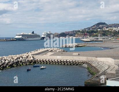 navi da crociera ormeggiate nella zona del porto di funchal a madeira, vicino alla città, con piccole imbarcazioni da pesca vicino al molo di cemento Foto Stock