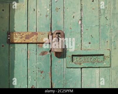 primo piano di una vecchia porta di legno con vernice sbiadita verde e un lucchetti chiuso arrugginito e vecchia letterbox in metallo Foto Stock