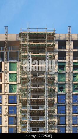 moderno edificio di appartamenti a più piani in costruzione con impalcature e telai di paranco sotto un cielo blu Foto Stock