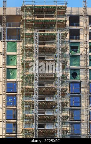 alto e moderno edificio di appartamenti a più piani in costruzione con impalcature e telai di paranco sotto un cielo blu Foto Stock