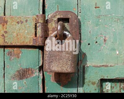 primo piano di un vecchio lucchetto in metallo arrugginito che fissa una barra di ferro su una porta di legno verde Foto Stock