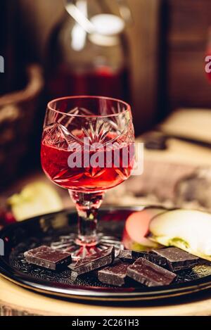 Bicchiere di ribes rosso in casa nalivka con fette di mela e cioccolato sulla piastra di metallo Foto Stock