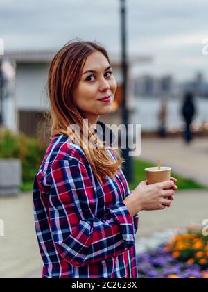 Caffè sul andare. Bella giovane donna azienda tazza da caffè e sorridente nel parco Foto Stock