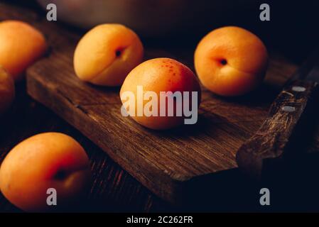 Mellow albicocche con il coltello su un vecchio tagliere di legno e metallo ciotola con frutti Foto Stock