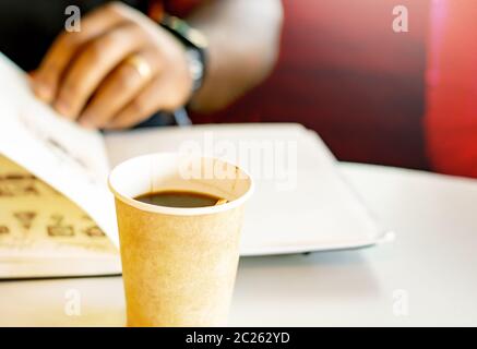 Una tazza di caffè con un uomo nero che legge un libro Foto Stock