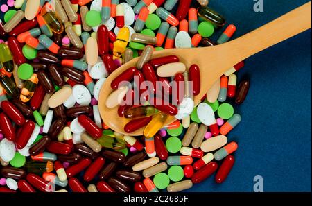 Pila di coloratissimi compresse e capsule pillole e cucchiaio di legno su sfondo blu. La resistenza agli antibiotici concetto. Industria farmaceutica. Healthca globale Foto Stock