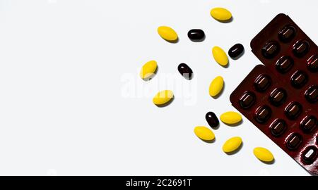 Macro shot di giallo compressa ovale pillole, nero compresse pillole su sfondo bianco con disegno creativo e nero caplet pillole in marrone confezione blister. P Foto Stock
