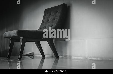 Nero sedia classica con design unico nella vuota stanza di riposo vicino al muro di cemento sulla oscura e drammatica dello sfondo. Premuto, triste e solitaria concetto. Uno e Foto Stock