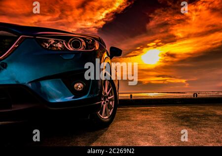 Blu compatte auto SUV con lo sport, moderna e design di lusso parcheggiato sulla strada concreta da parte del mare al tramonto. Vista frontale della bella vettura ibrida. La guida w Foto Stock
