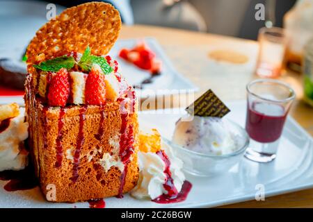Miele di topping toast con fragole, un lato di panna montata, gelato alla vaniglia. Tostare il pane sul piatto bianco su sfondo sfocato di lava di cioccolato c Foto Stock