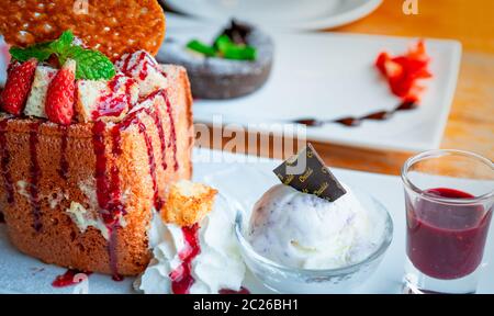 Miele di topping toast con fragole, un lato di panna montata, gelato alla vaniglia. Tostare il pane sul piatto bianco su sfondo sfocato di lava di cioccolato c Foto Stock