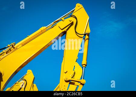 Giallo retroescavatore con pistone idraulico braccio contro il cielo blu e chiaro. Macchina pesante per lo scavo nel sito in costruzione. Macchine idrauliche. Enorme infrangere Foto Stock