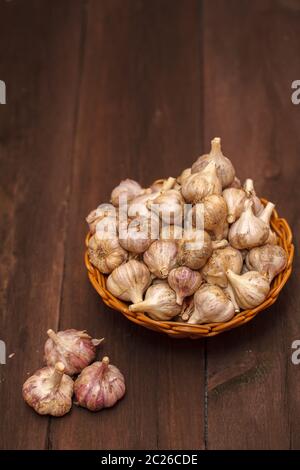 teste di aglio in un cesto di vimini su un legno Foto Stock