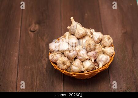 teste di aglio in un cesto di vimini su un legno Foto Stock