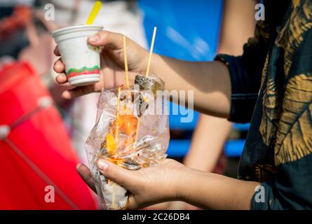 Le donne mangiano calamari arrostiti con salsa di pesce in sacchetto di plastica trasparente insieme al gelato in tazza di plastica Foto Stock