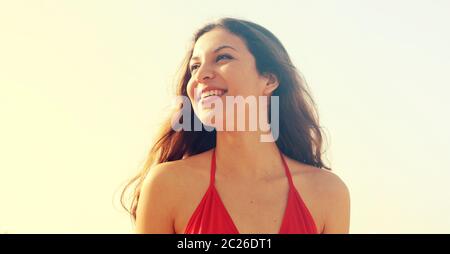 Bella bruna in bikini rosso sorridente fiducioso e guardando al lato sulla spiaggia in una giornata di sole basso angolo raccolto banner Foto Stock