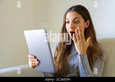 Ragazza felice che usa il tablet. Donna entusiasta che tiene il tablet pc sul divano a casa Foto Stock