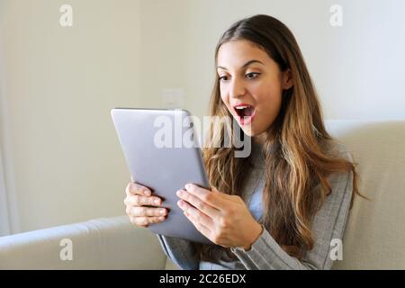 Ragazza felice che usa il tablet. Donna entusiasta che tiene il tablet pc sul divano a casa Foto Stock