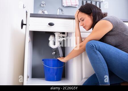 Preoccupato della donna la raccolta di perdite di acqua dal lavello in blu la benna Foto Stock