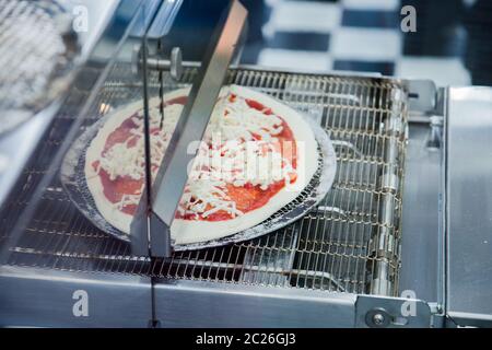 Ready-made pizza italiana su sottile pasta cotti in attrezzatura speciale. Messa a fuoco selettiva. Foto Stock