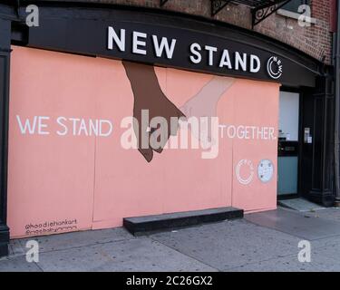 New York, NY - 16 giugno 2020: Ci stiamo in piedi insieme e graffiti di mani in bianco e nero visti su compensato coperto New Stand store su Bowery Foto Stock