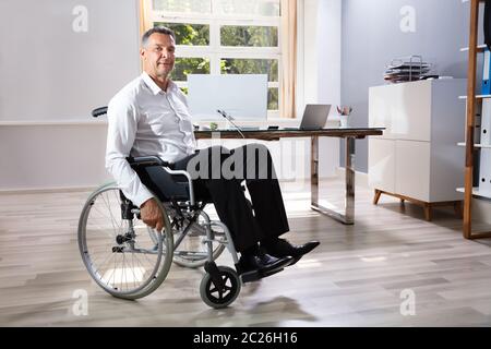 Imprenditore disabile seduto su una sedia a rotelle in Office Foto Stock