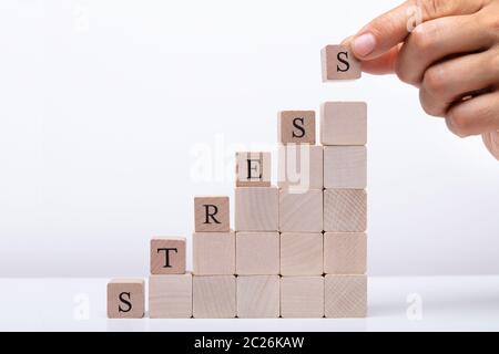 Persona della mano che trattiene i blocchi di legno ponendo ultimo alfabeto della parola Stress sulla scrivania bianca Foto Stock