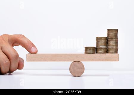 Close-up di un imprenditore la mano di bilanciamento delle monete impilate su altalena in legno con il dito sulla scrivania Foto Stock