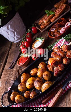 Datteri rustici avvolti in pancetta e patate giovani arrostite. Foto Stock