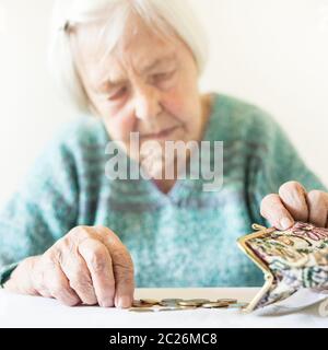In questione anziani 96 anni vecchia donna seduta a tavola in casa e il conteggio delle monete rimanenti dai regimi pensionistici nel suo portafoglio dopo il pagamento di fatture. Unsustainabi Foto Stock