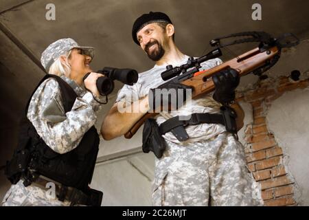 Sorridenti uomini e donne allegri militari stanno tenendo crossbow e binocoli al chiuso. Foto Stock