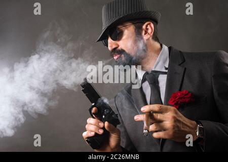 L'elegante boss mafia o gangster è fumare sigaro e tenere la pistola in mano. Foto Stock