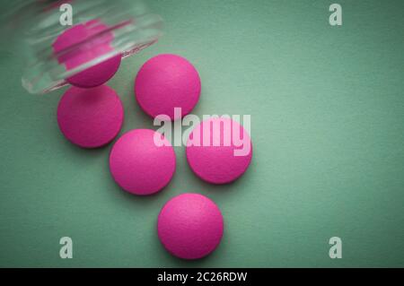 Le compresse di colore rosa sono versata da un vaso di vetro su uno sfondo verde Foto Stock