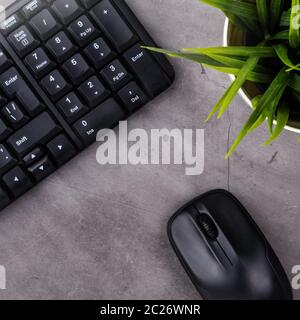 Luogo di lavoro sulla tabella scuro con copia spazio. Tavolo con tastiera e mouse del computer, fiori in vaso. Lay piatto. Vista dall'alto, i raggi del sole dal lato Foto Stock