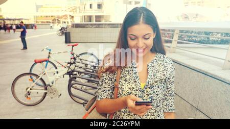 Ritratto di un attraente giovane donna utilizzando uno smartphone. Dirigenti che lavorano con un telefono cellulare per la strada. Panoramica vista banner. Desatured retrò Foto Stock