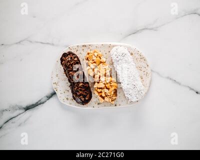 Set di tre eclair fatti in casa su sfondo di marmo. Vista dall'alto di deliziosi profittole salutari con diversi elementi di arredo - cioccolato, arachidi e frassino Foto Stock