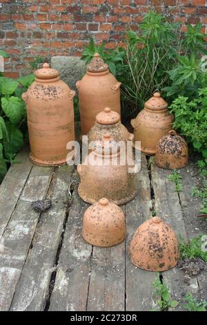 Vasi di rinbaro in terracotta con coperchi su vecchio ponte di legno con muratura in mattoni e piante come sfondo. Foto Stock