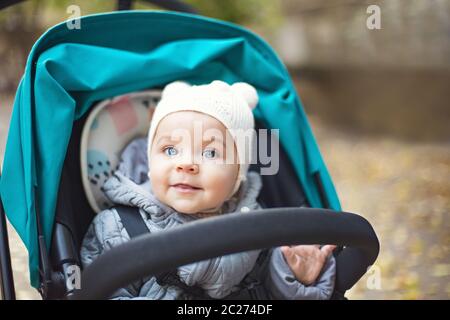 Felice bambino carino in un passeggino che guarda fuori e ridendo nel parco Foto Stock