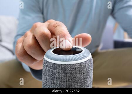 L'uomo premendo il pulsante su altoparlante wireless a casa Foto Stock