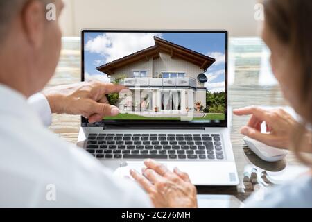 Vista posteriore di due imprenditori in cerca di casa su computer portatile Foto Stock