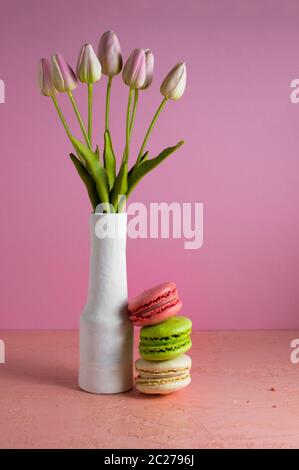 Amaretti su un pallido sfondo rosa accanto a un vaso di tulipani. Posto per il testo Foto Stock