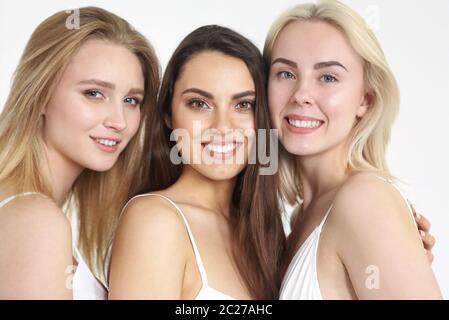 Gruppo di donne felici e diverse in bianco abbracciando su sfondo bianco. Foto Stock