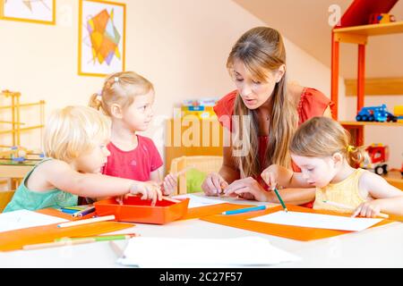 Bambini che disegnano in un gruppo di gioco della scuola materna con l'aiuto dell'insegnante Foto Stock