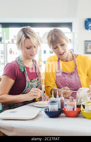 Due amiche dipinto loro ceramiche fatte a mano in un workshop hobby Foto Stock