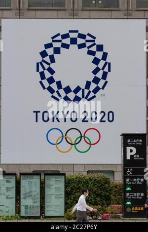 Un salarista giapponese passa davanti all'edificio del governo metropolitano di Tokyo con il logo per le Olimpiadi di Tokyo del 2020, Shinjuku, Tokyo, Giappone Foto Stock