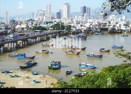 Colorate barche da pesca in legno ancorate in una trafficata via d'acqua con un moderno skyline in lontananza in una giornata di sole a Nha Trang, Vietnam, il 3 giugno 2020. Foto Stock